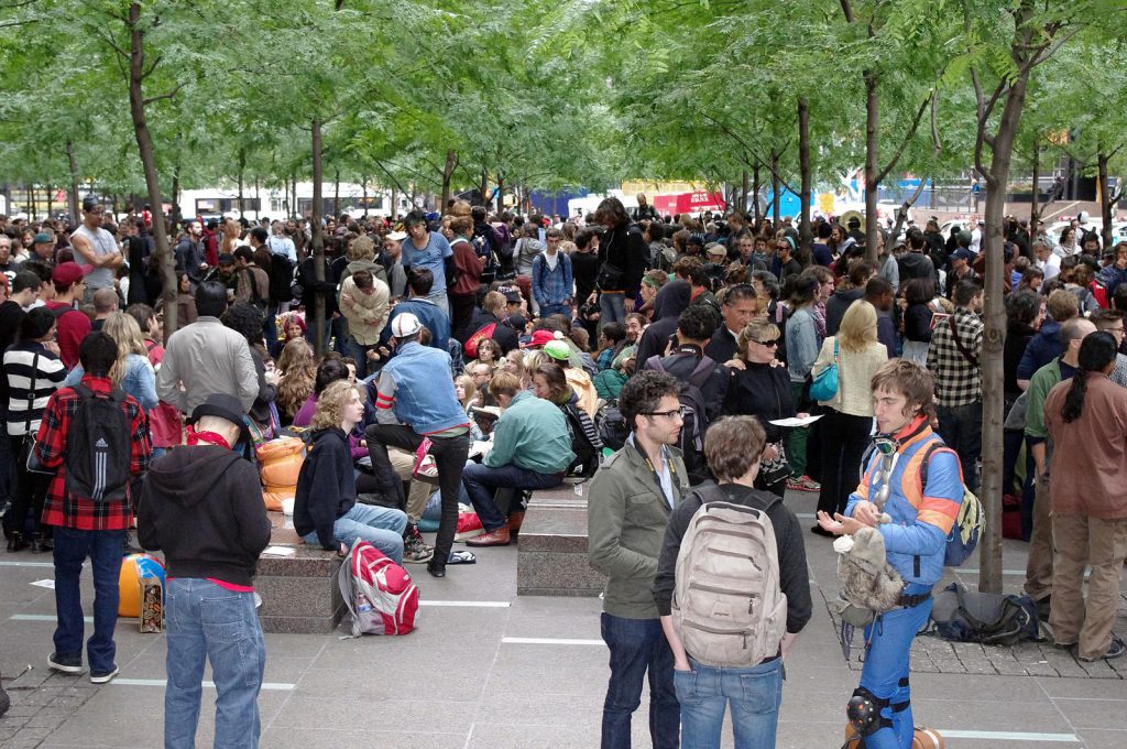 People gather in a square, many in conversation in small groups.
